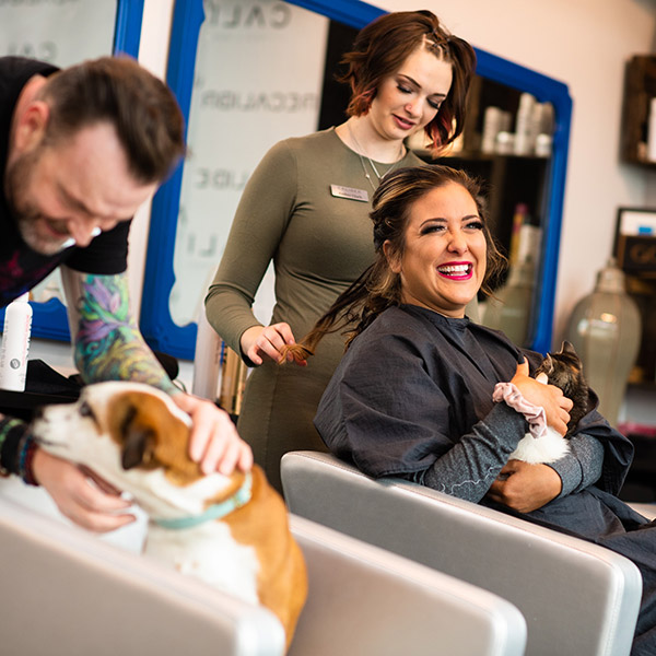 Stylist doing women's hair and man playing with dog